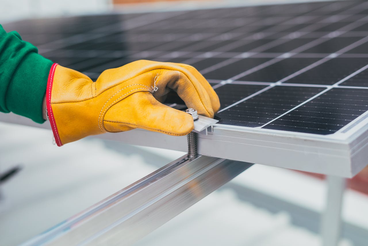 Close-up of a worker's hand with protective gloves adjusting a bolt on a solar panel.