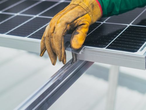 Close-up of a worker's hand in protective glove installing a solar panel.
